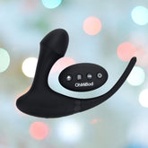 A curved and ergonomic black vibrator made from body-safe silicone, with a three-button remote control, both from the OhMiBod Club Vibe 3.OH Hero Vibrating Anal Plug by OhMiBod, set against a blurred, colorful bokeh background.